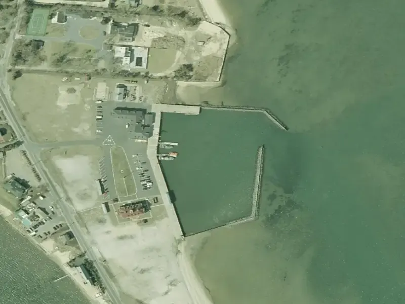 Aerial frame of the Shinnecock Bay demo site, 2001: a small harbor basin with a stone breakwater, a beach and buildings on the west shore, open bay water to the east.
